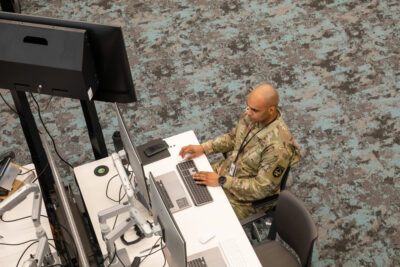 |奥斯汀社区学院区 A top view of a male soldier with a shaved head in Army camo sits at a computer at the 军队软件厂